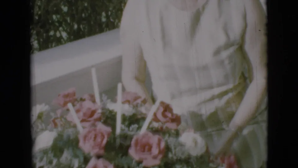 In the final frame, the woman stands on the porch behind a floral arrangement with pink roses and light-colored candles or stems.