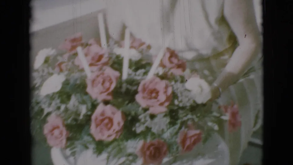 A woman in a light dress works over a rose bouquet on a porch in 1966 Clarkdale footage.