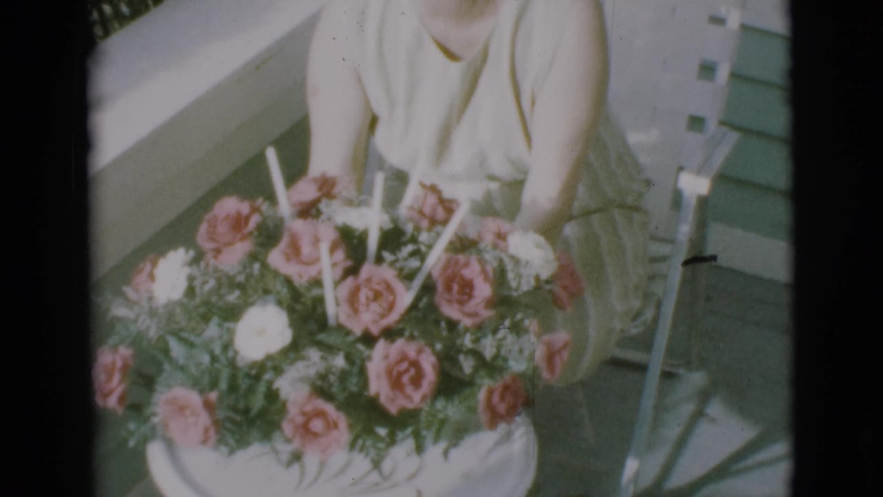 Woman holds a round table with a rose bouquet and candles on a porch.