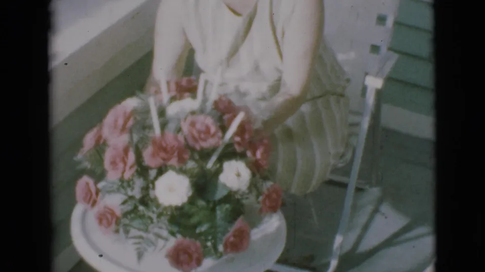 A seated woman in Clarkdale, Arizona, continues rotating a bouquet of roses and greenery on a small white table in 1966 footage.