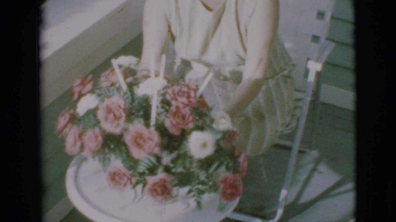 Large floral arrangement with pink and white flowers in front of a seated woman on a porch chair.