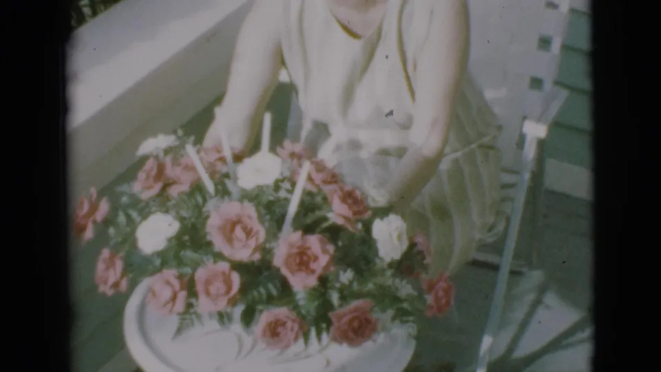 A woman in a light dress sits on a porch chair while handling or adjusting a large bouquet in 1966 Clarkdale footage.