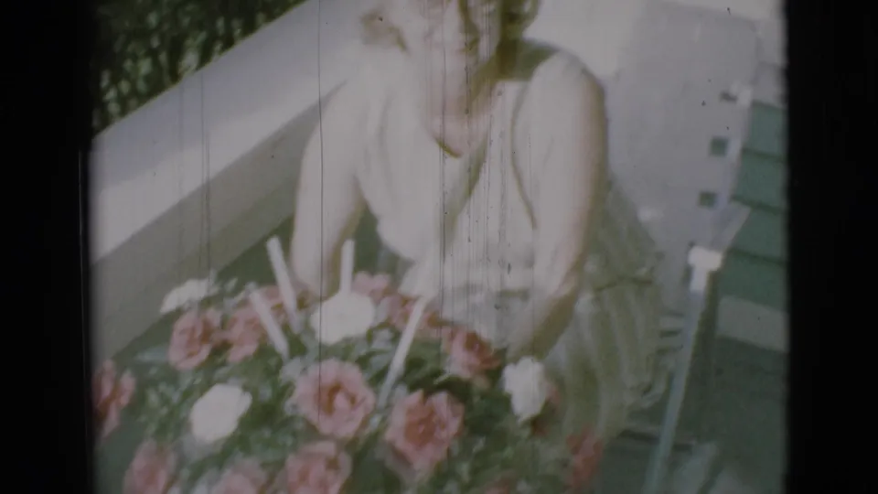 A smiling woman sits behind a large flower arrangement on a porch in 1966 Clarkdale, Arizona home-movie footage.