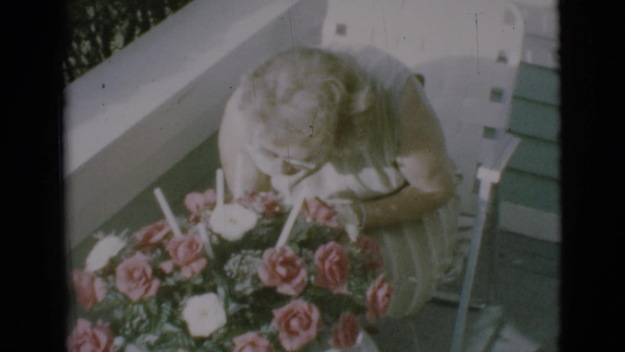 On a Clarkdale porch in 1966, the woman leans forward to smell pink and white roses on a table.