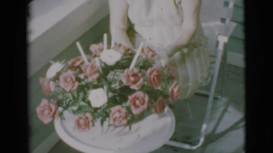 A large pink and white rose arrangement dominates the porch scene, with the woman partly cropped behind it in 1966 Clarkdale footage.