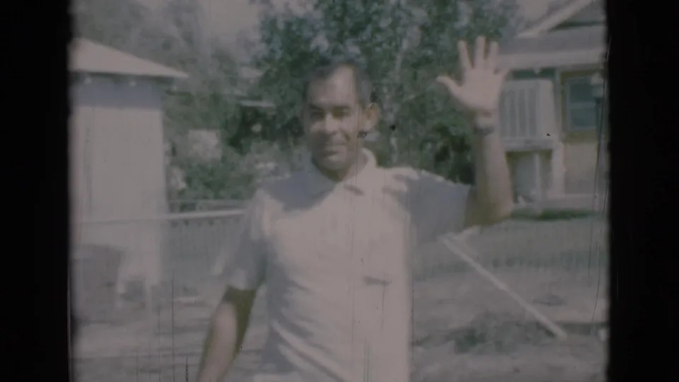In 1966 Clarkdale home-movie footage, a man in a light polo smiles and waves toward the camera in a sunny yard.