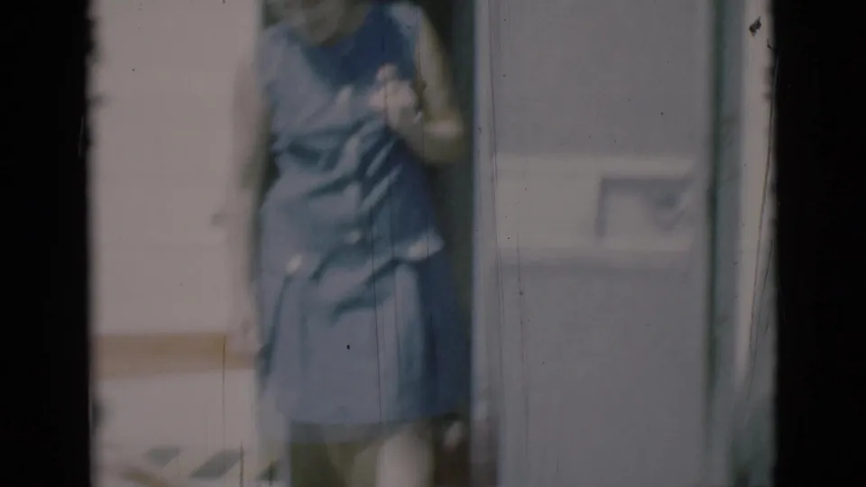 A woman in a blue sleeveless dress is partly framed by the camper doorway in the 1966 home-movie footage.
