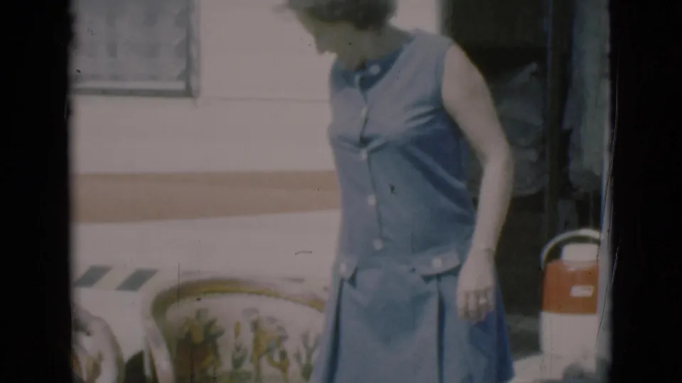 A woman in a blue sleeveless dress steps from a camper in Clarkdale, with a red-and-white cooler visible nearby.