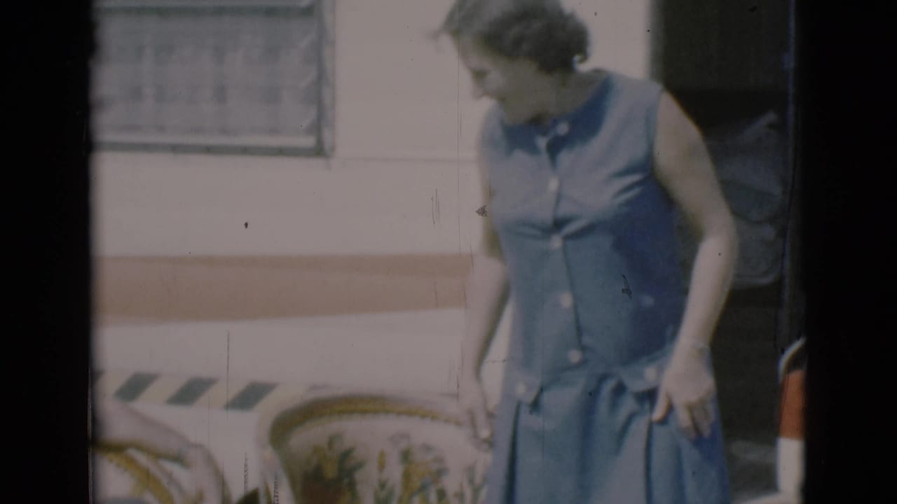 Woman in a sleeveless blue dress standing beside a camper and lawn chair.