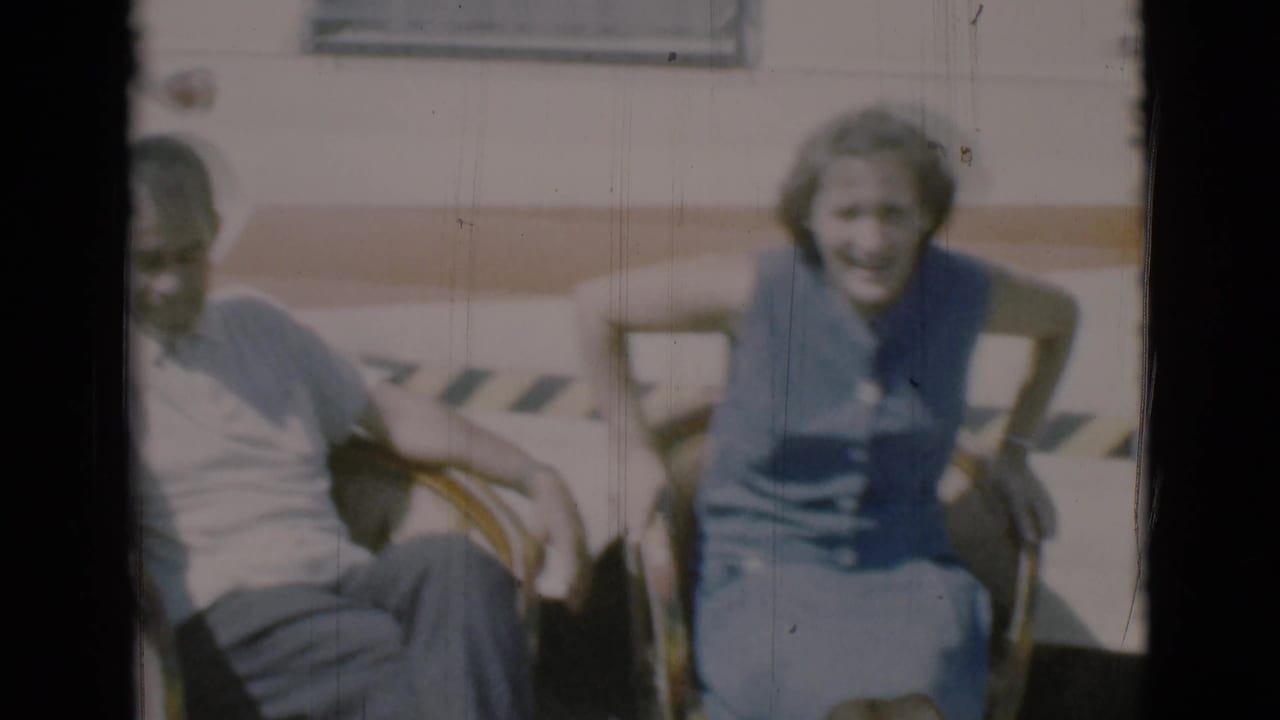 Man and woman seated in lawn chairs beside a light-colored camper.