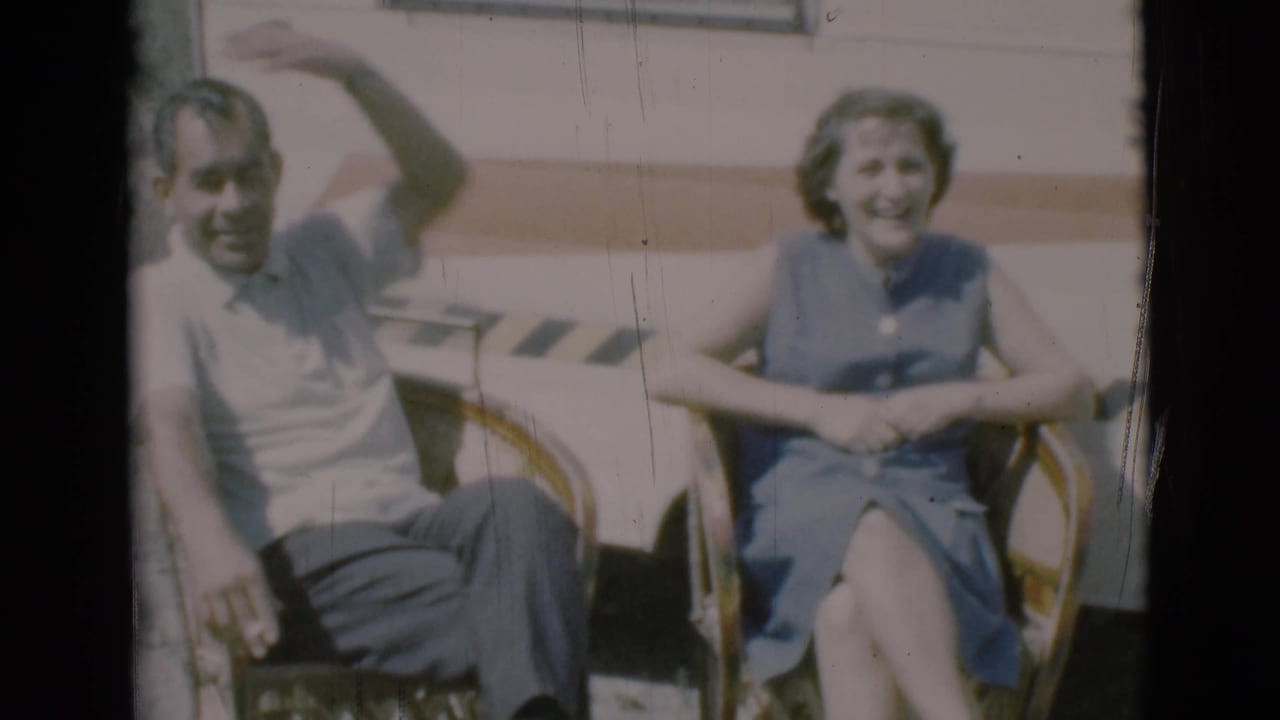 Adult couple seated in wicker chairs outside a caravan wall.