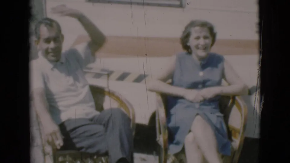 In Clarkdale, Arizona, a 1966 8mm frame shows an adult couple seated outdoors in wicker chairs beside a caravan.
