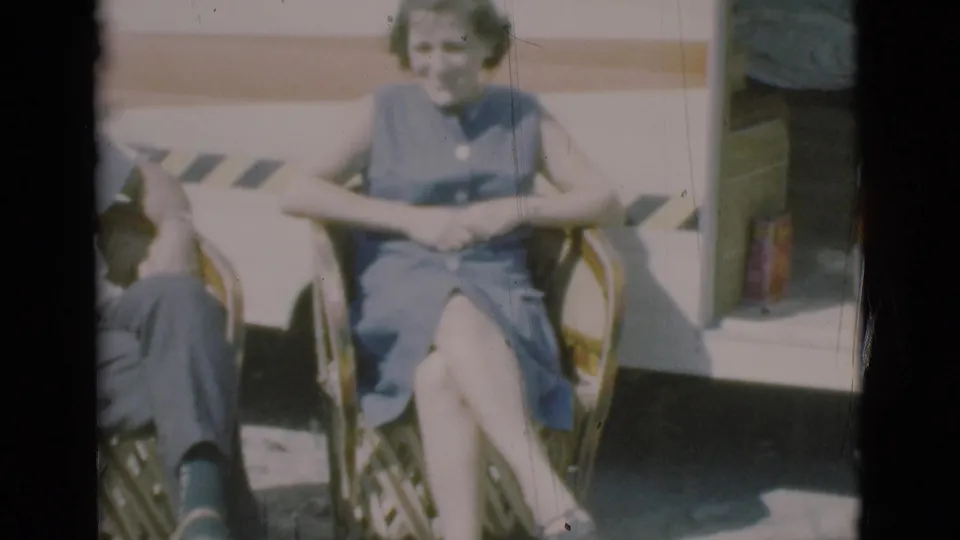 A soft 8mm frame shows the woman seated outside the caravan while the man is mostly cropped from the left side.