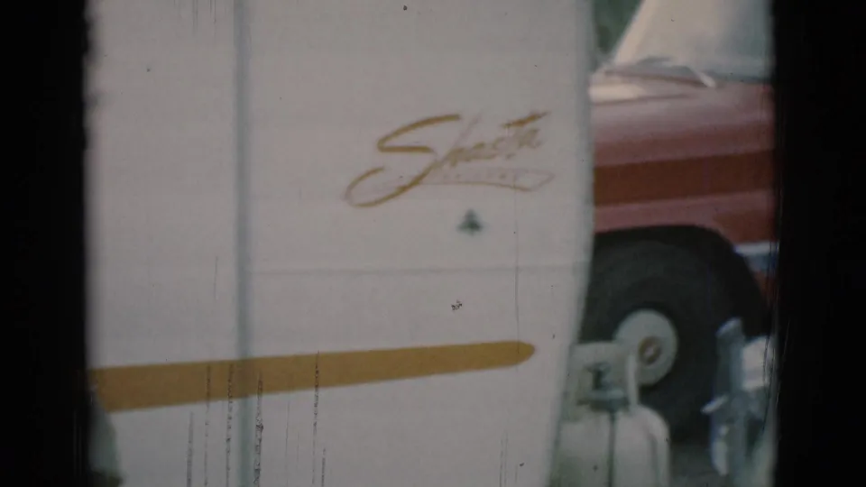 1966 Clarkdale, Arizona home-movie frame showing a white Shasta trailer, gold stripe, propane tank, and part of a red vehicle.