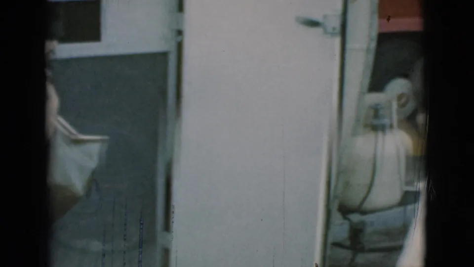 The trailer doorway remains in frame with a partial bag, propane tank, gold side stripe, and red vehicle visible in the background.
