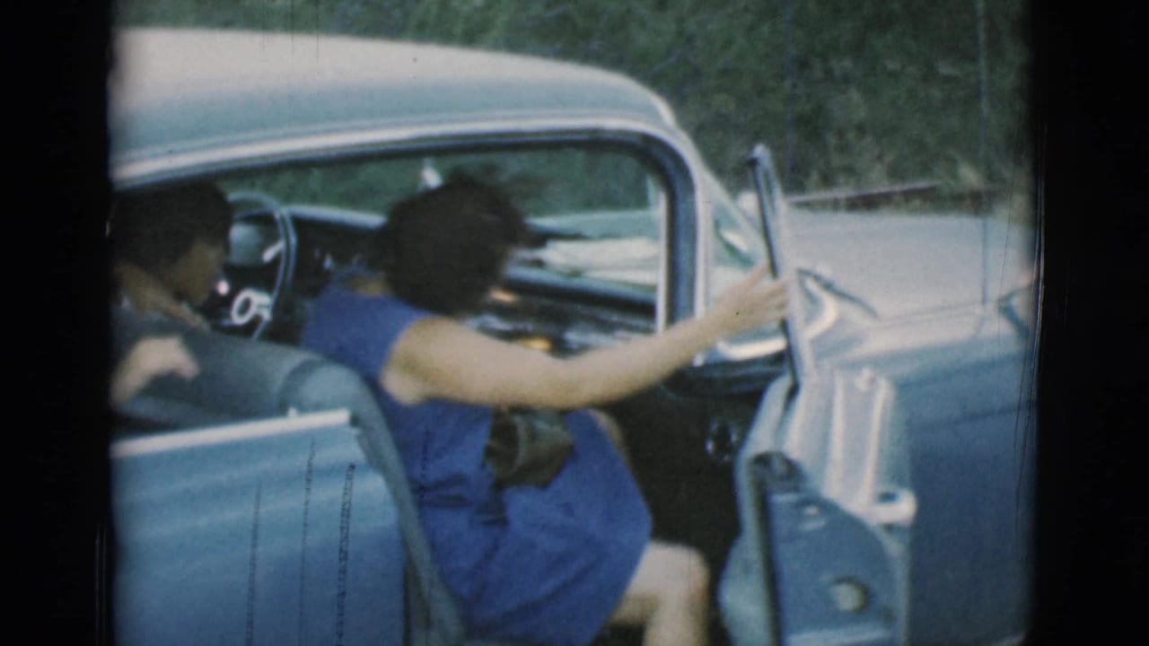Woman in a blue dress entering the driver side of a blue vintage car.