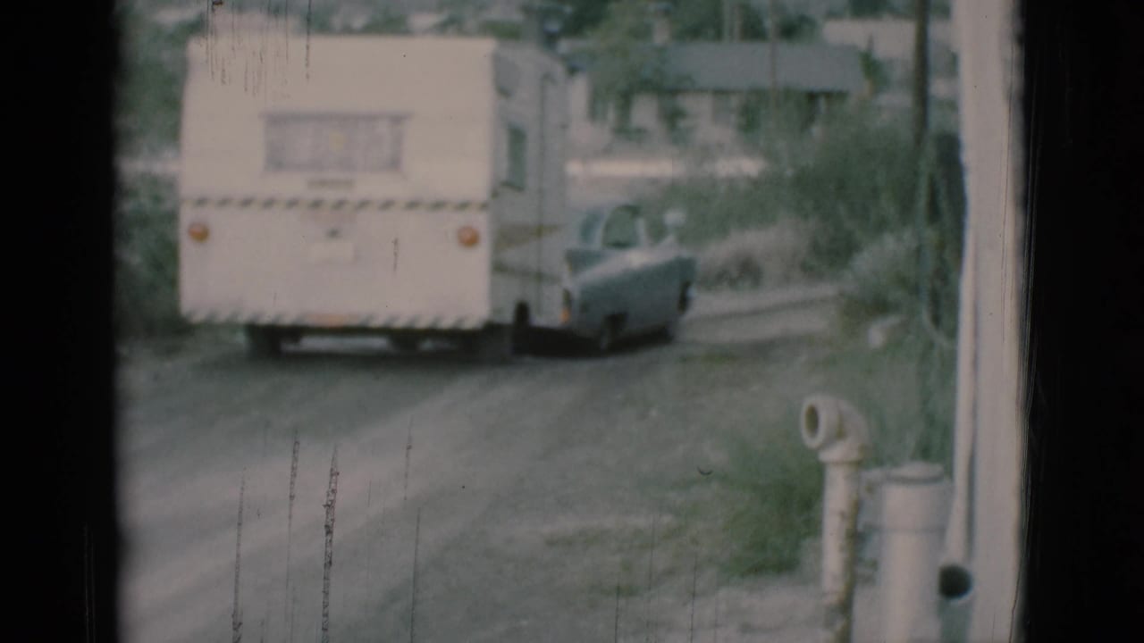 White caravan trailer towed by a gray sedan continues along a dirt road in the 1966 Clarkdale home-movie footage.
