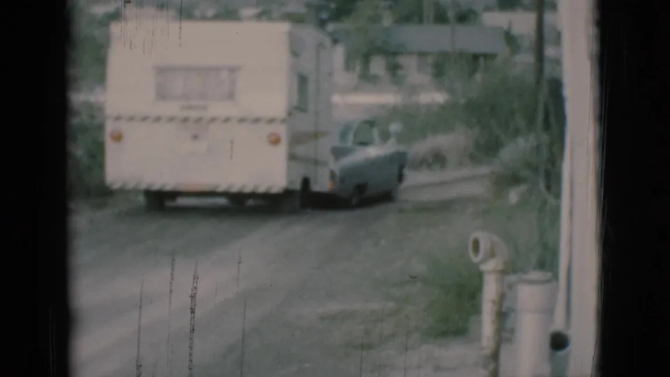 White caravan trailer towed by a gray sedan continues along a dirt road in the 1966 Clarkdale home-movie footage.