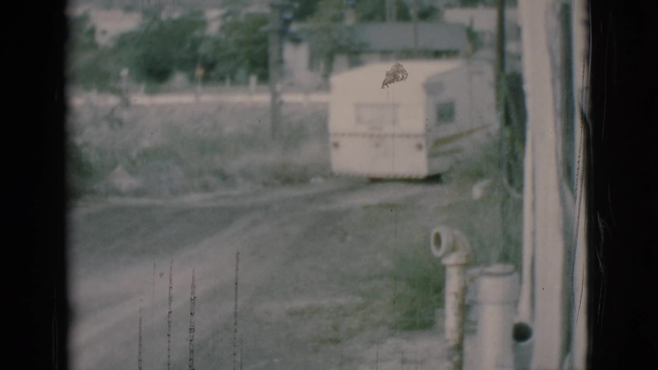 White camper trailer parked near a dirt road beyond a window frame.