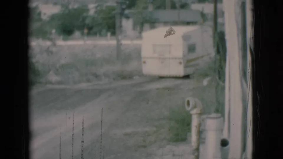 1966 Clarkdale 8mm frame showing a white camper trailer on a dirt road outside a residence, seen through a dark window edge.