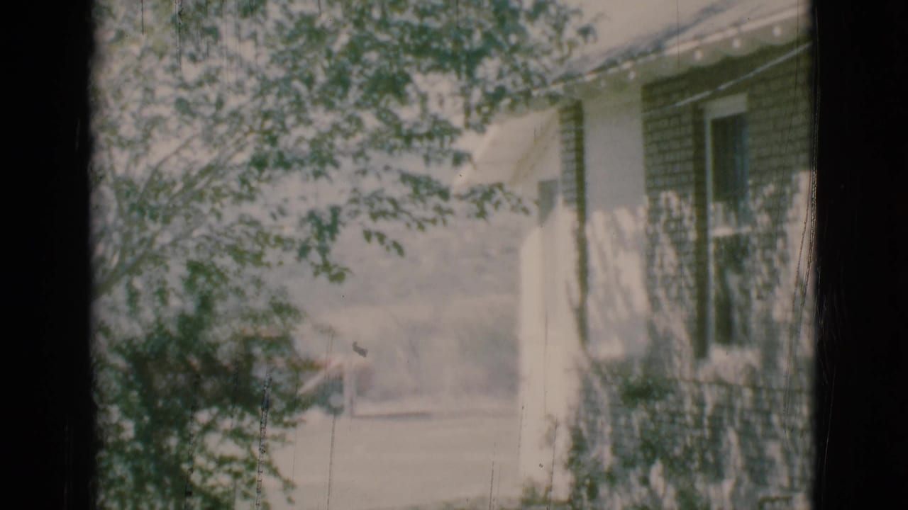 House exterior partly hidden by leafy branches and a dark vertical frame.