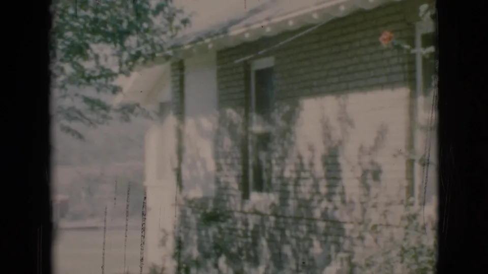 Soft 8mm view of a Clarkdale house exterior with dark shingles, a pale porch post, railing, and leafy shadows across the facade.
