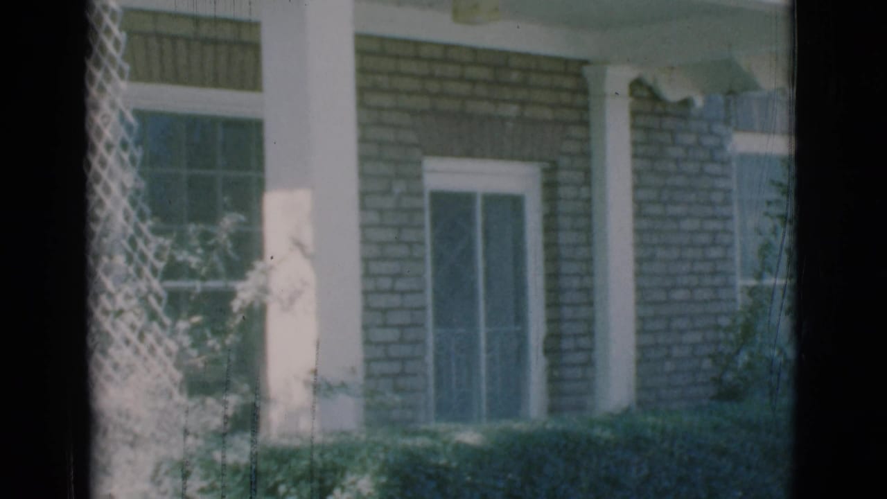 Brick house exterior with white porch pillars, screened windows, hedges, and a dark vertical window edge.