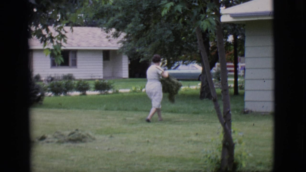 Woman carries a large bundle of lawn clippings across the grass.