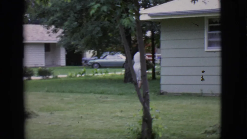 Near the end of the 1966 Clarkdale clip, the woman moves partly out of view beside a house and trees in the yard.