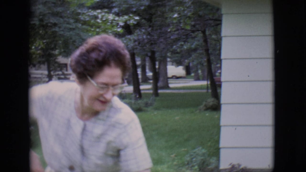 Woman in glasses looks down beside a porch with a lawn and trees in the background.