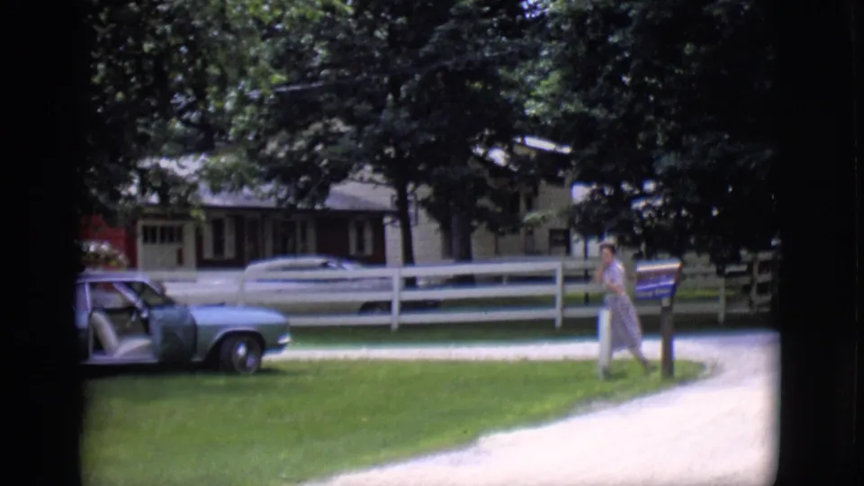 In Clarkdale, Arizona, a woman crosses a grassy suburban yard toward a light blue classic car in 1966 home-movie footage.
