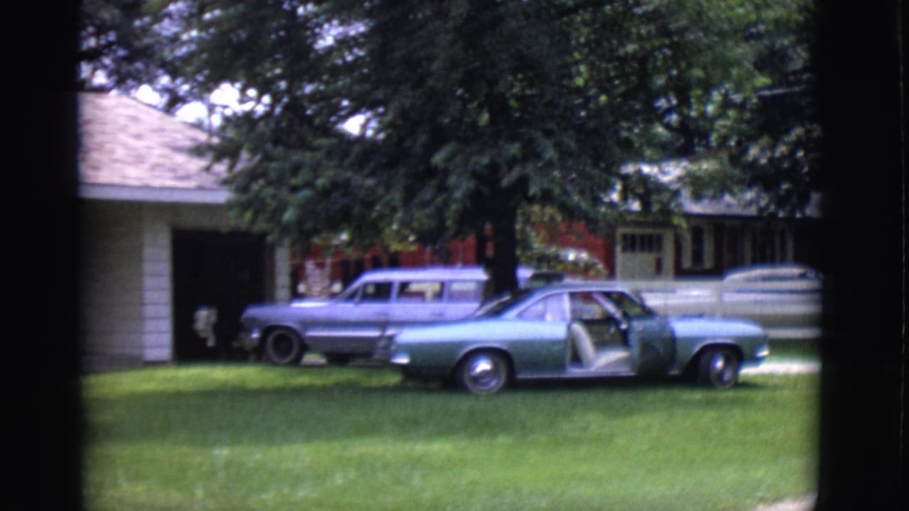 1966 Clarkdale home-movie frame showing a white-sided house, lawn, trees, a station wagon, and a teal coupe with its door open.