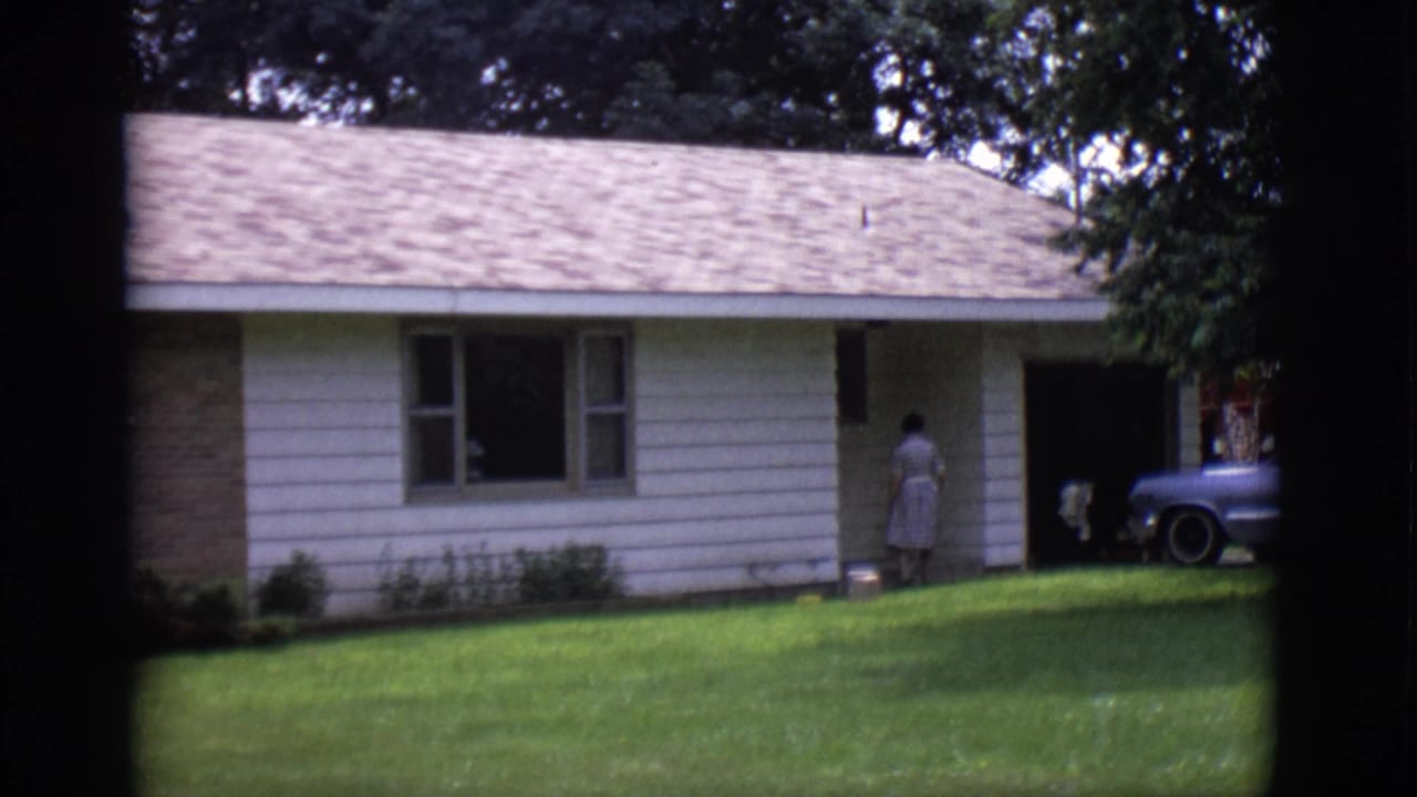 1966 Clarkdale, Arizona frame with a woman turned toward the entrance of a ranch-style house and a station wagon partly visible.