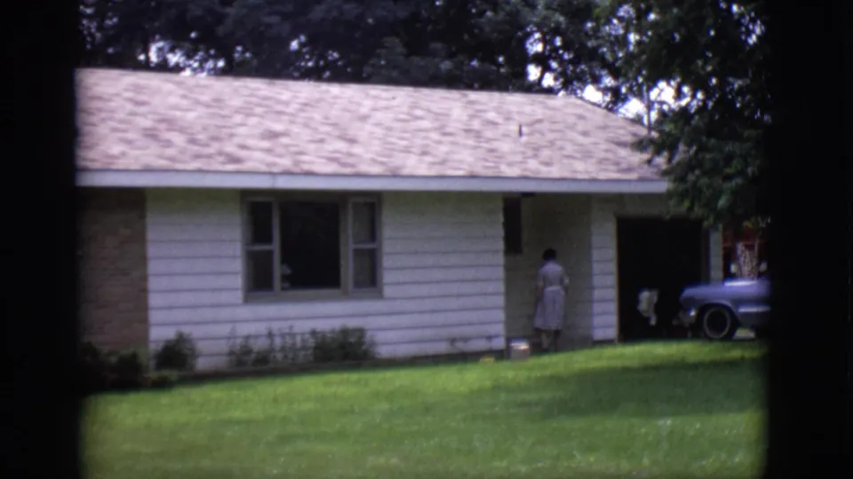 1966 Clarkdale, Arizona frame with a woman turned toward the entrance of a ranch-style house and a station wagon partly visible.
