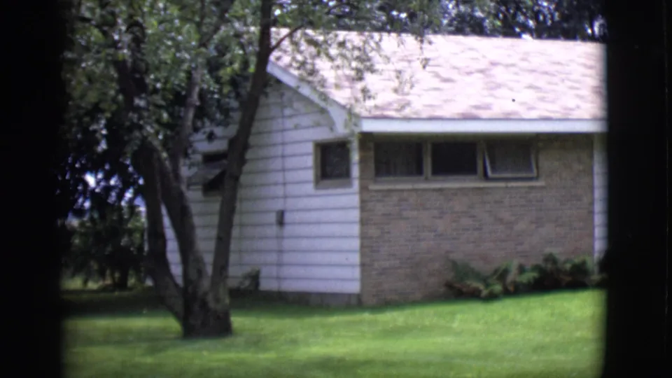 1966 Clarkdale, Arizona 8mm frame showing the ranch house exterior partially obscured by tree trunks in the foreground.