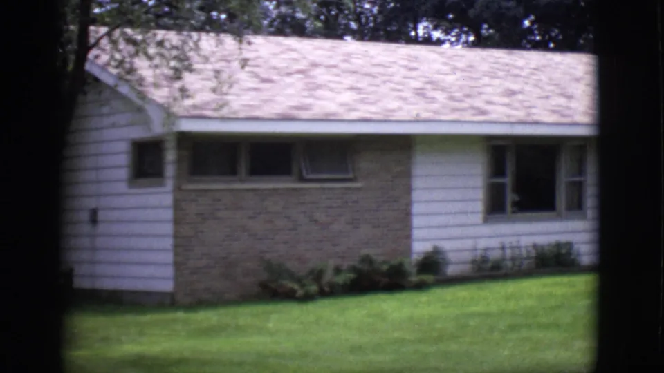 1966 Clarkdale, Arizona 8mm frame showing the front wall of a ranch-style house with brick, white siding, windows, shrubs, and lawn.