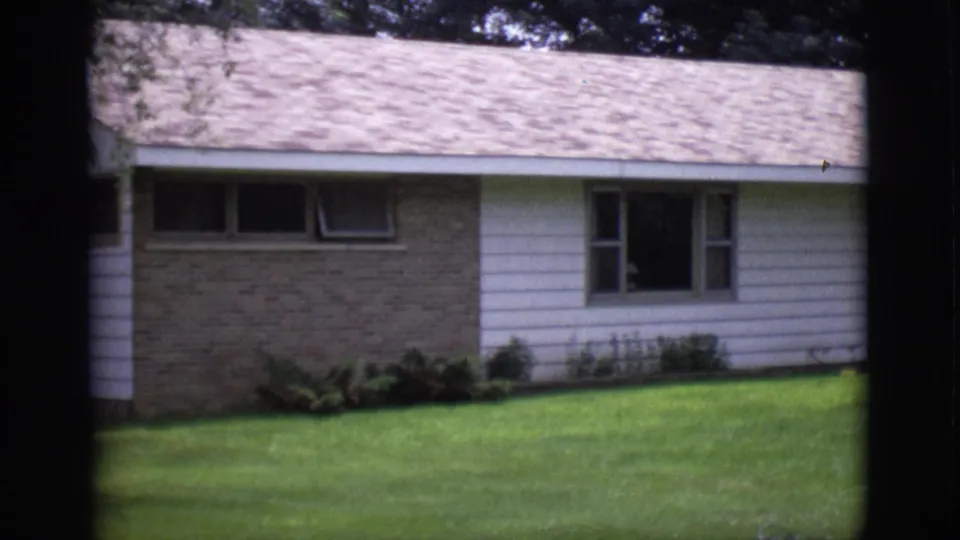 Clarkdale, Arizona 1966 home-movie frame showing a ranch-style house facade, brick accent wall, windows, shrubs, and broad front lawn.
