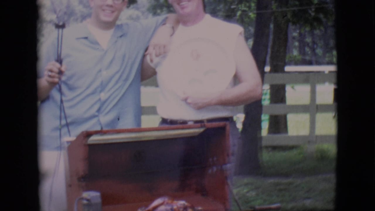Two men stand partly cropped behind a red grill, with one holding a round object.