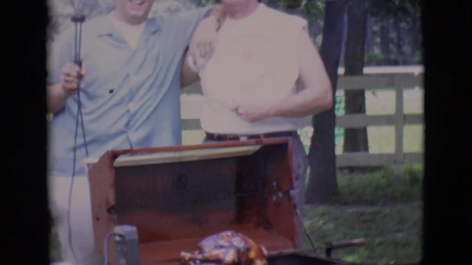 A closer cropped 1966 home-movie view shows the men above the red grill and roast on the spit below.