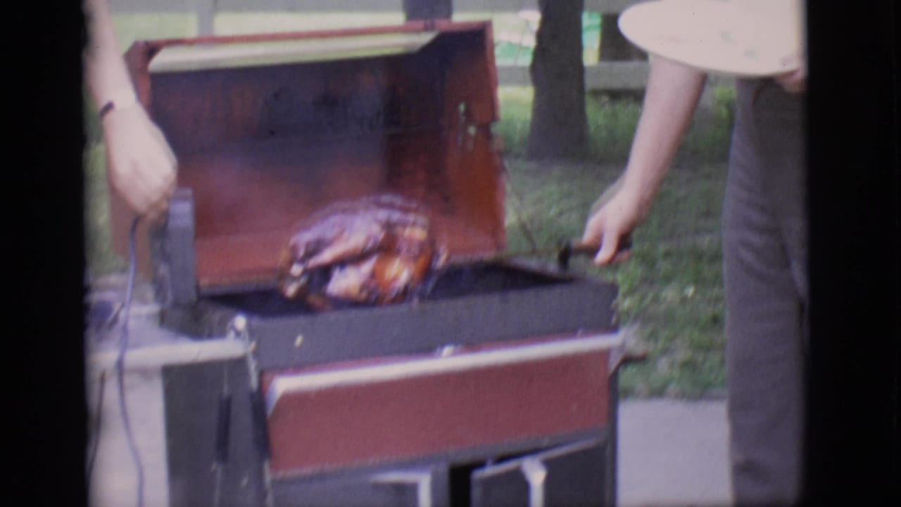 Man beside an open rotisserie grill with a roasted turkey on the spit.