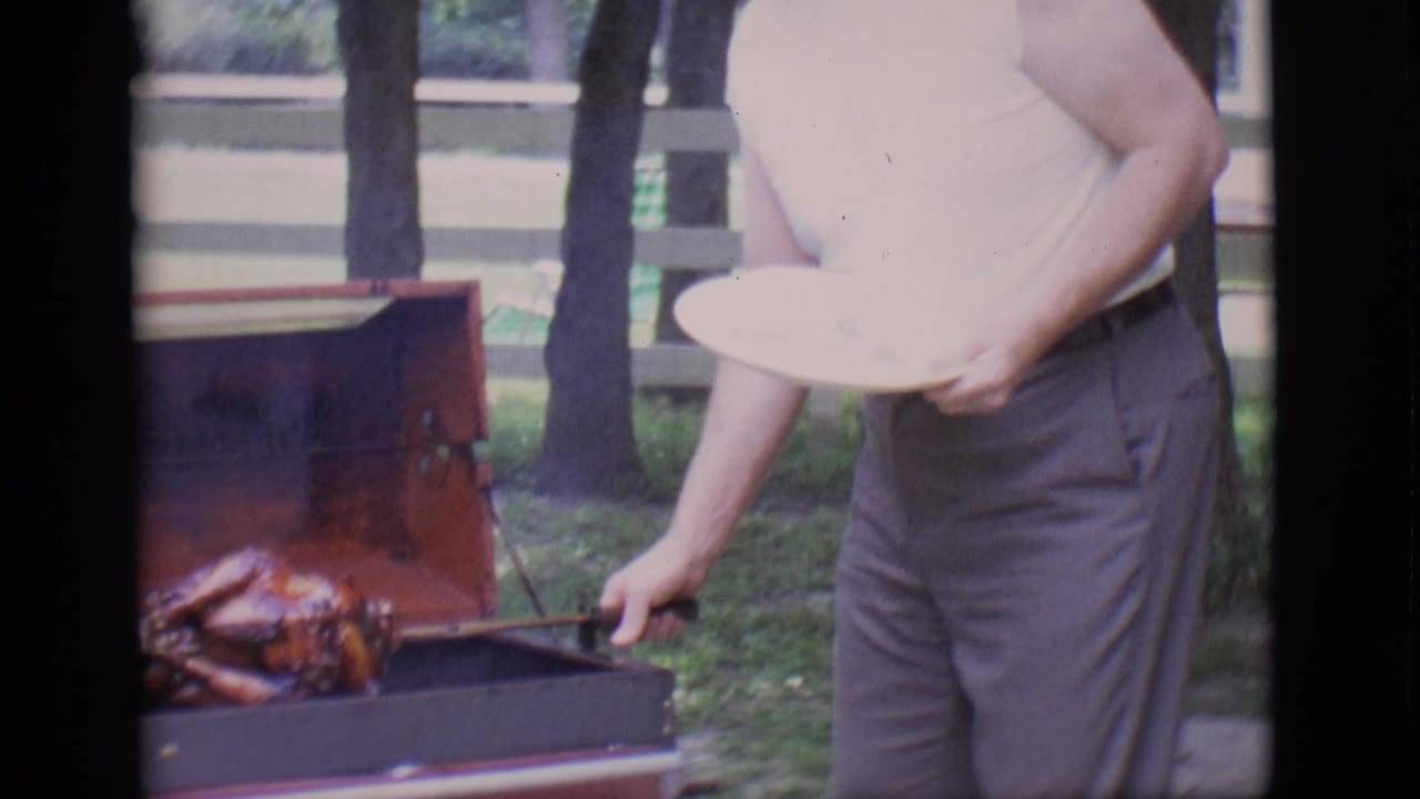 Man holds a plate while adjusting the spit on a backyard grill.