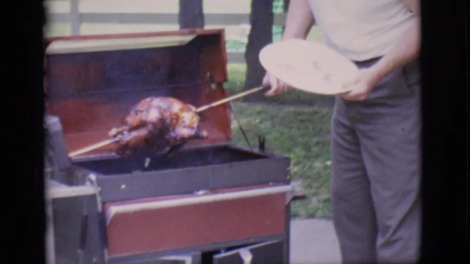 A man steadies the spit and plate as the roasted turkey is lifted over the open backyard grill in Clarkdale, Arizona footage.