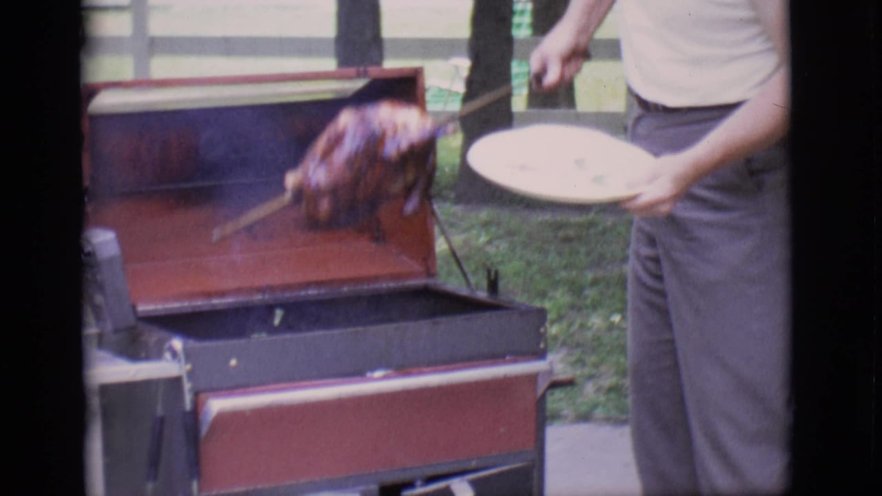 Roasted turkey is lifted from the open grill while a man holds a white plate nearby.