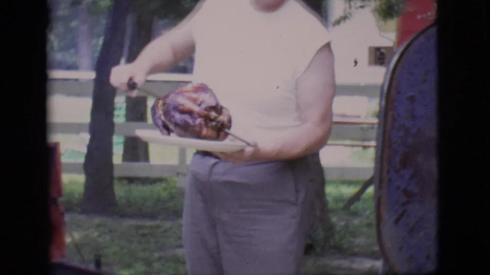 The man holds the plated roasted turkey in the Clarkdale backyard, with trees, grass, and a fence behind him.