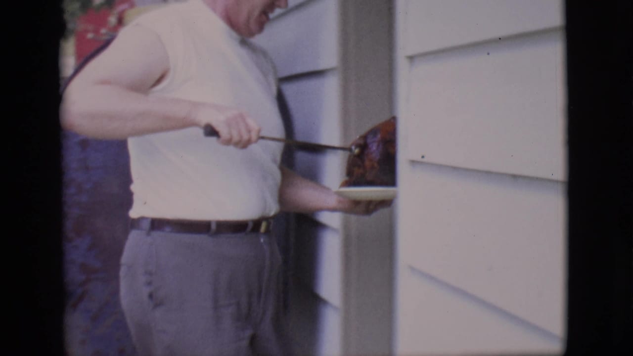Man carries the cooked bird on a plate from the grill toward a house doorway.