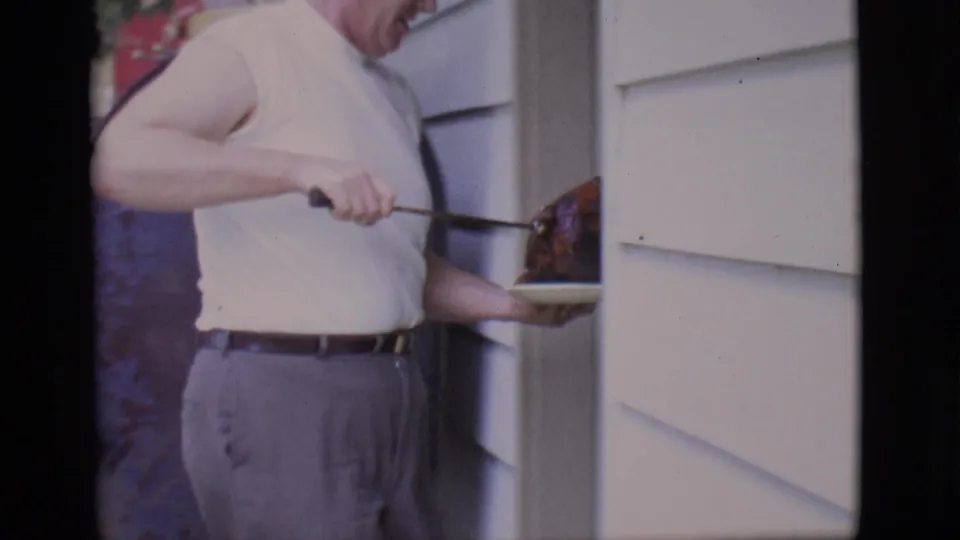 The man carries the roast on a white plate past siding and a large blue tank in the 1966 Clarkdale home-movie scene.