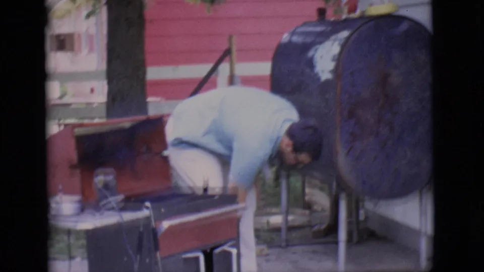 A man bends near the backyard barbecue area in Clarkdale, with the red grill, patio furniture, and blue tank visible.