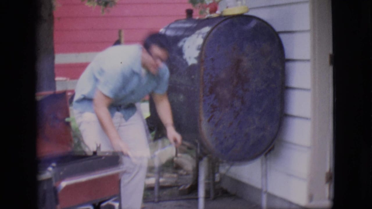 Man bends beside a red grill near a large black outdoor smoker.
