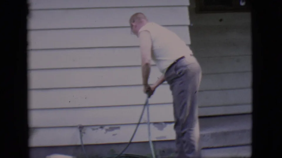 The hose task continues as the man bends near the foundation of the white-sided house in 1966 Clarkdale footage.