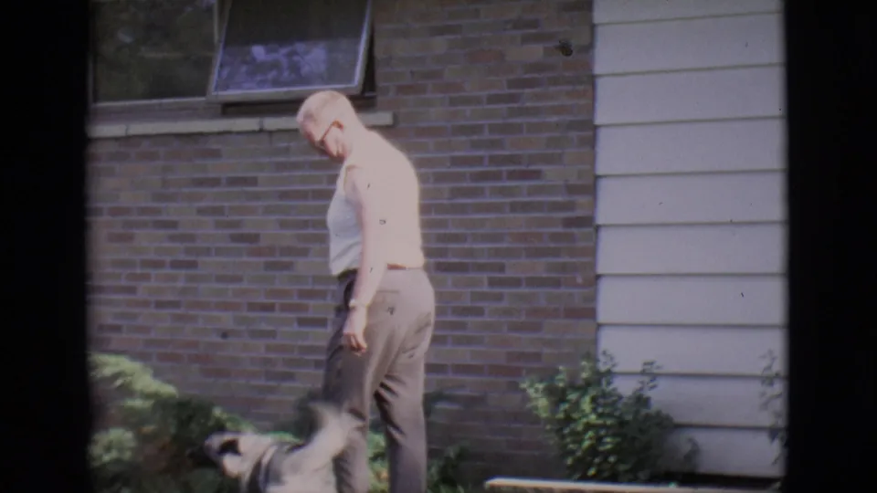 A light-colored dog approaches the man on the lawn beside the Clarkdale house exterior.